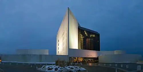 A white triangular tower rises beside a black glass building, with circular structures on either side.