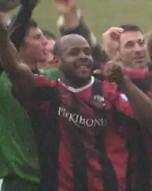 Black footballer and a cluster of others all smiling and waving