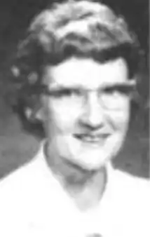 A middle-aged smiling white woman wearing short wavy hair and glasses, and a white collared shirt