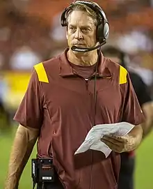 Color photograph of white man wearing a red shirt and audio headset.