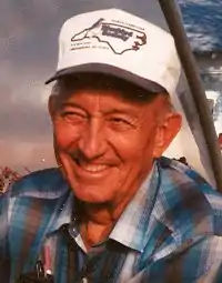 Portrait of Mister Jack Finch, an elderly man wearing a big smile, a baseball cap and plaid shirt