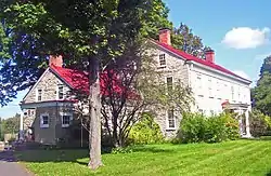 A stone house with red roof and a tall tree in front