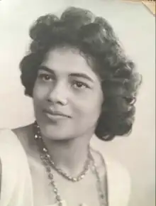 A young woman with brown skin and coiffed hair, wearing a strand of shiny beads