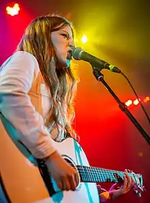 Woman performing onstage against a purple background