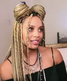 The woman in the photo, Jade Novah, has blonde box braids, hoop earrings, light brown skin, and green eyes