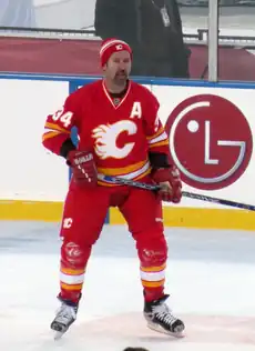 A hockey player in a red uniform with yellow and white trim and matching toque.  The logo on the chest is a white stylized "flaming C"