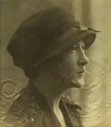 A young woman in an early 20th century American style hat and blouse looks to the viewers' right