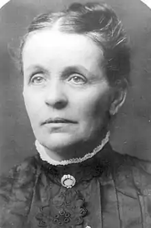 Black-and-white image of a woman in late middle age with tied-up hair, in formal Victorian dress