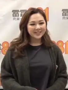 East Asian woman with shoulder-length hair wearing dark top and cardigan, smiling left of camera