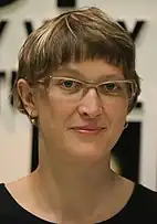 A 35-year-old woman with brown and blonde hair and glasses smiling at the camera.