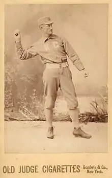 A baseball player is standing in his uniform, with his arm extended in the act of throwing a baseball.