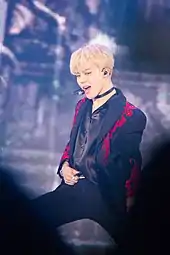 Jimin stands on a stage holding his belt while dancing.