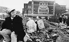 Black and white photograph of Joan Littlewood sat on rubble outside the Theatre Royal, Stratford, East London