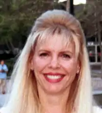 a tight headshot of a light skinned woman with bright red lipstick and blonde hair. She is smiling.