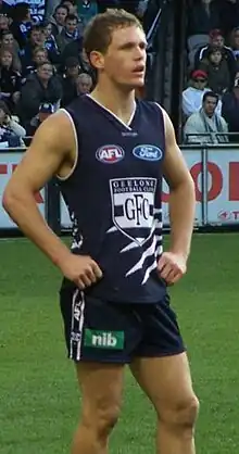 A brown-haired male athlete wearing a navy sleeveless jersey and shorts