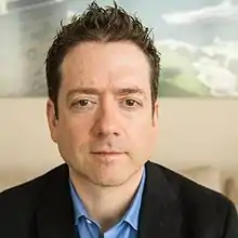 Portrait of author, seasteading evangelist Joe Quirk with short, dark hair wearing a blue shirt and blazer