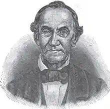 A man with receding black hair, a high-collared white shirt, and a black jacket and bowtie