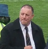 Photo of a man in a black coat and black tie