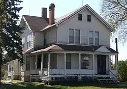 Two-story wooden house with wrap-around porch and two chimneys