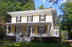 A yellow house partially in sunlight with wide roof eaves and a front porch