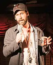 man in checked jacket and baseball hat with microphone