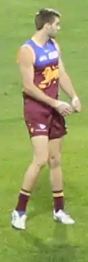 A man in a maroon football jersey stands on grass.