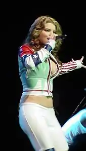 A woman is performing a song over the stage. She wears a white jacket and pants.