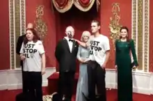 Two people, wearing Just Stop Oil t-shirts, stand in front of wax sculptures.