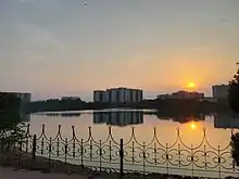 A lake surrounded by a path and fence with apartments. The sun is setting.