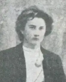 A young white man with longish tousled hair, wearing a dark jacket and a white shirt