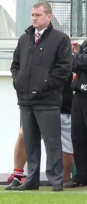 Karl Marginson, F.C. United's longest serving manager, stands at the side of a football pitch watching the game.