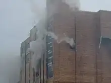 Upper portion of brick building with smoke pouring from windows