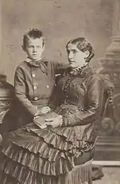 A young woman facing left sits with a child to her right