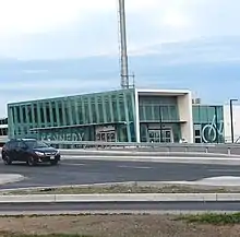 A photo of a glass panelled light rail station with the name "Kennedy" in bold white lettering on the side. The structure is mostly completed, but signage over the entrances has not yet been added.