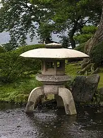 Three legged yukimi-dōrō. One leg rests on ground, two in water.