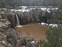 Landscape above the canyon walls is also visible, gently sloping toward steep 40 ft. cliffs, showing the abrupt nature of the geologic sink.