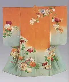 A peach- and light blue-grey coloured kimono with medium-length sleeves viewed from the back. It has a single crest just below the collar at the back, and is lined in light pink. The kimono is woven with an abstract design of bamboo shoots, with the fabric beginning as a light blue-grey on the hem before graduating into a strong peach colour at the top. The kimono is decorated with a hand-painted design of flowers and plants.