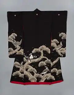 A black kimono with long sleeves viewed from the back. The kimono has three crests along the back and is lined in scarlet and has a thickly-padded hem. A painterly design of pine trees is seen across the bottom of the sleeves and from the waist down. Hawks are depicted as perching on the thick branches.