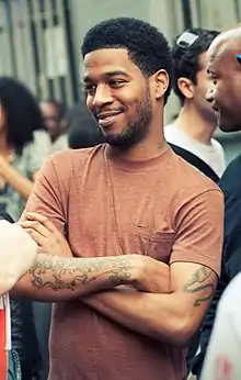 A man in a brown t-shirt, with hands folded.