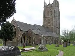 Gray stone building with ornate square tower and slate roof. In the foreground are gravestones.