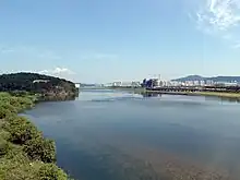 A vast and tranquil river in a clear day of fall. Apartment blocks and buildings under construction are seen at a distance.