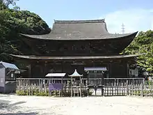 Large wooden building with and added enclosing pent roof.