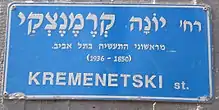 The blue Israeli street sign is in Hebrew. Translated to English it says: "Yonah Kremenetski, one of the first industrialists in Tel Aviv (1850–1936)."