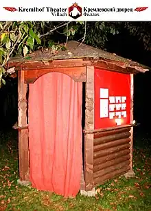 Photograph of the theatre entrance into a small wooden structure with a red cloth for a door