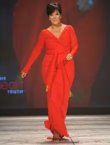 A woman in a red outfit and brown shoes walking on a stage while swinging her hands