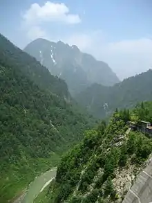 A deep mountain valley with a river and wooded slopes.