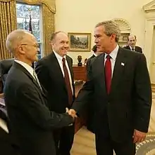 Bush shakes hands with Kydland with Prescott behind them.