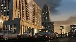 Several cars drive down a street in Los Angeles in 1947 in the evening, with several tall buildings in the background.