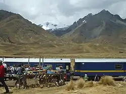 The train Belmond Andean Explorer at La Raya Station with market stalls and the mountain Chimboya in the background