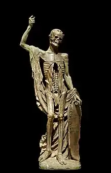 An alabaster statue showing Death as a living skeleton. His right arm is draped with a shroud and raised upwards. His skull appears to be looking downwards. His shield is inscribed with a verse in French.